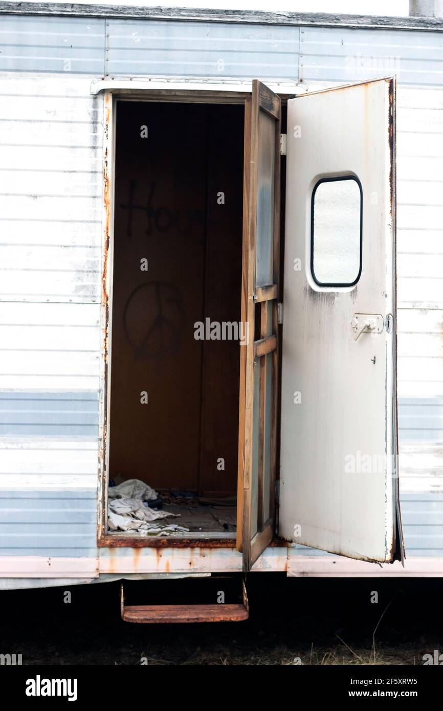 Old dilapidated blue and white single wide trailer that has been abandoned with door open Stock Photo