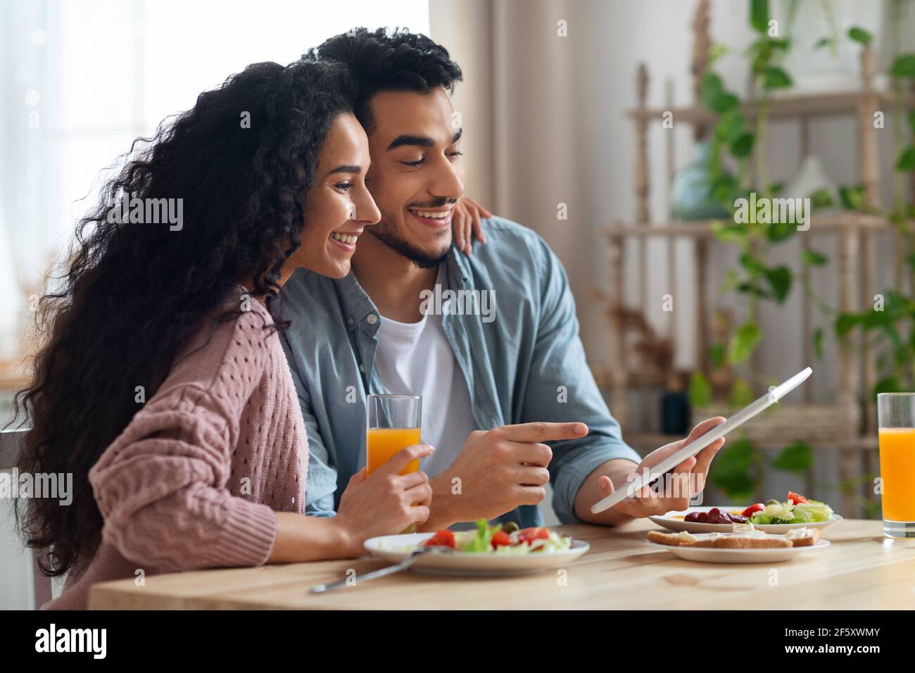 Young Arab Couple Using Digital Tablet In Kitchen While Having Breakfast Stock Photo