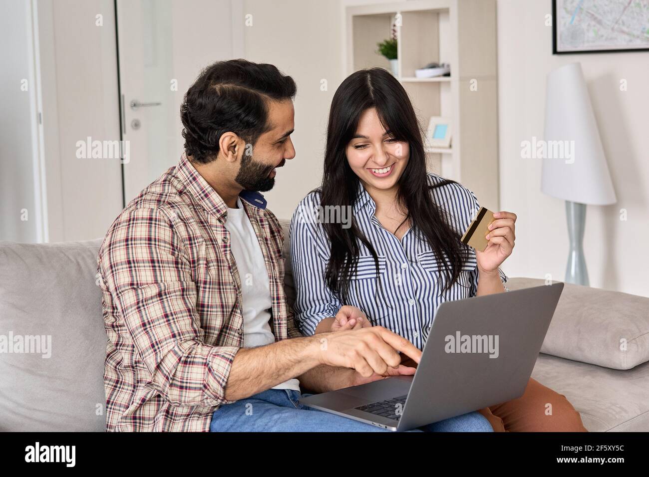 Happy indian couple shoppers doing online shopping using credit card and laptop. Stock Photo