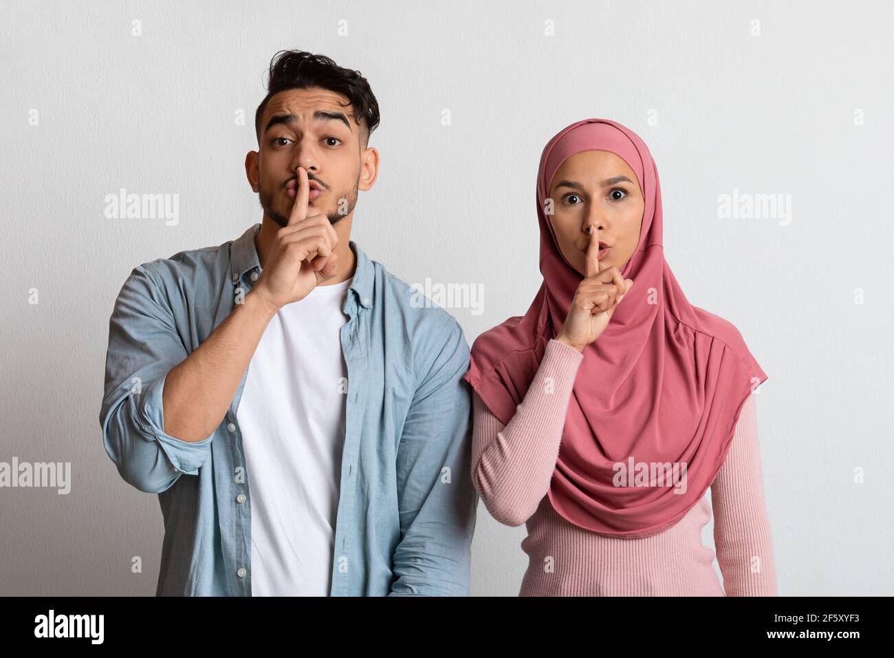 Young muslim couple making silence sign, keeping forefingers on lips Stock Photo