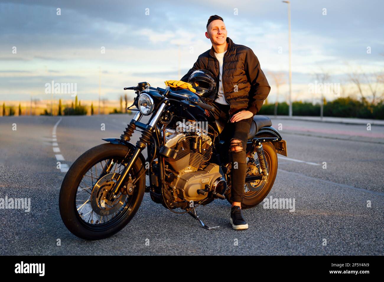 Man sitting on motorbike looking at horizon at sunset Stock Photo