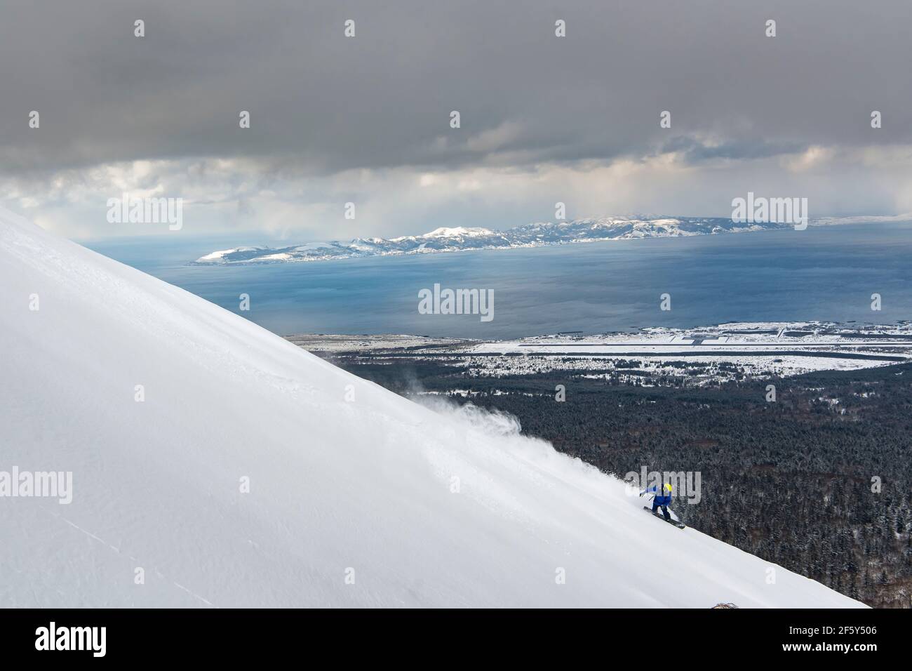 Person snowboarding on slope of snowcapped mountain against sky during winter vacation Stock Photo