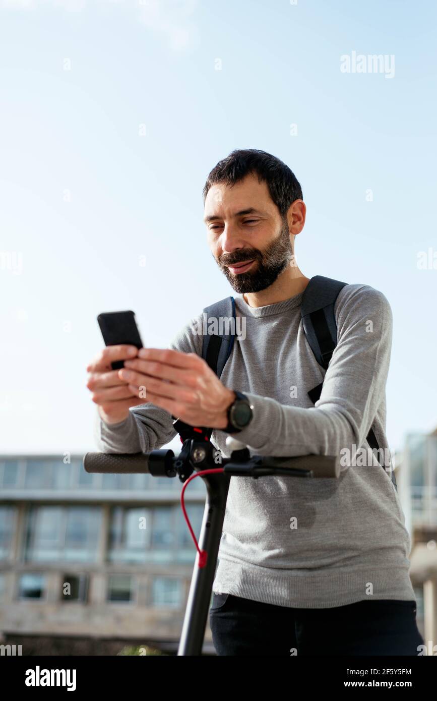 Young man standing on scooter and using smartphone Stock Photo