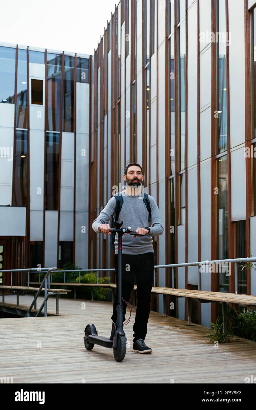 Young businessman commuting to work walking near electric scooter Stock Photo