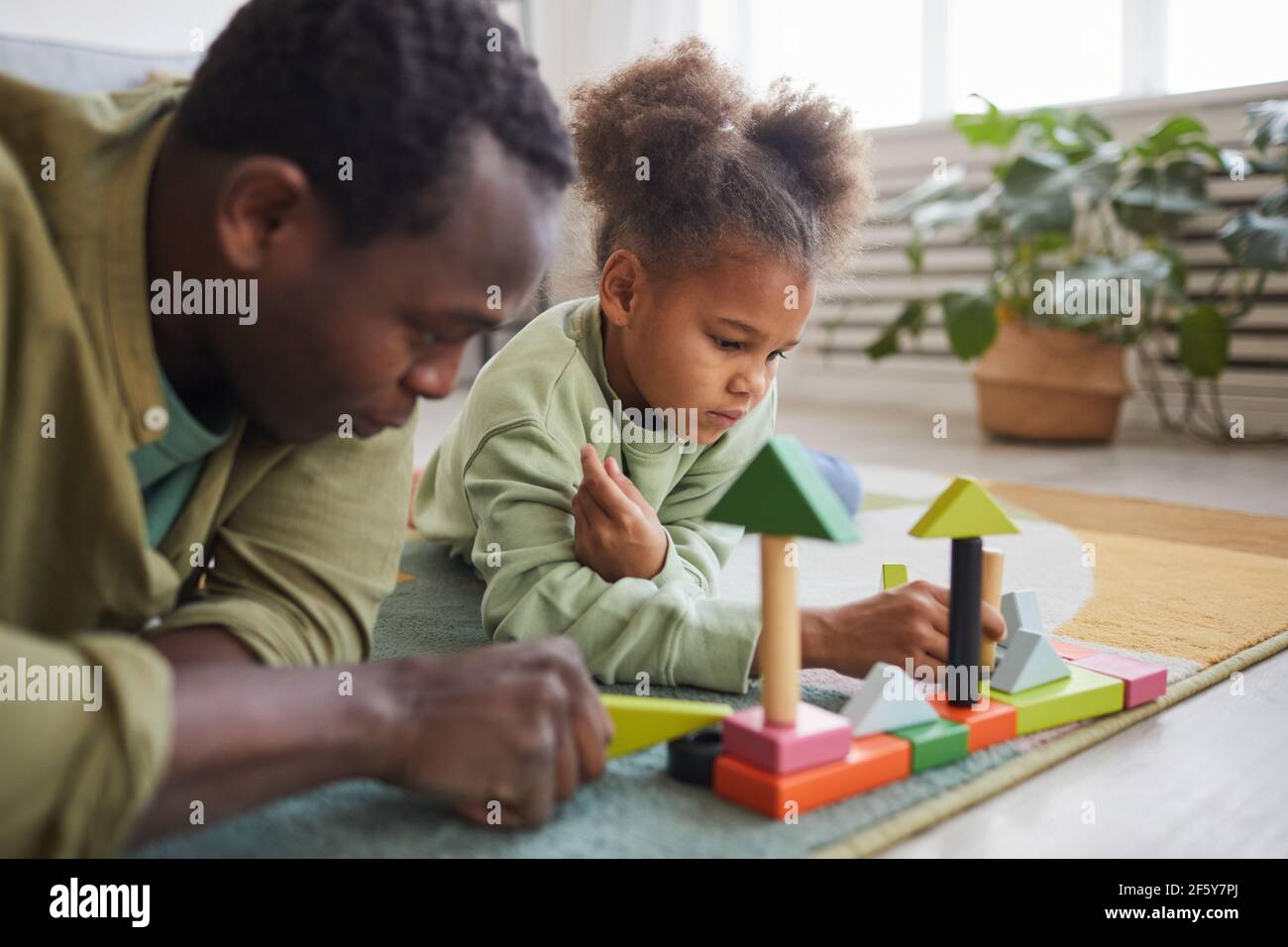 Portrait of African-American man playing with daughter while lying on floor in cozy home interior, copy space Stock Photo