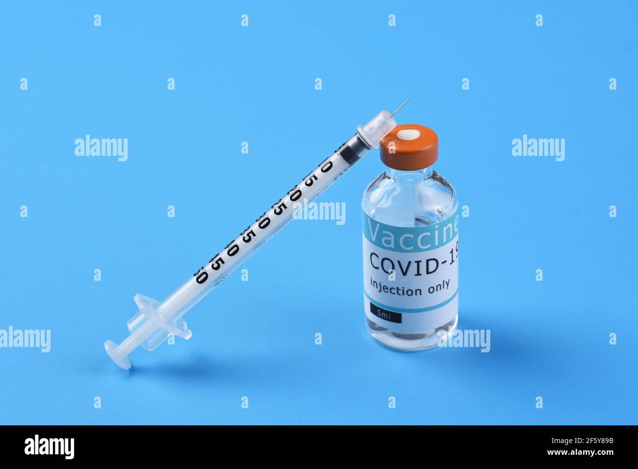 A vial of Covid-19 vaccine with a syringe leaning on the bottle on a blue background, with copy space. Stock Photo