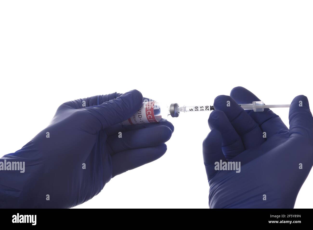 Closeup of two hands in surgical gloves with a syringe and vial of Covid-19 vaccine backlit over a white background. Stock Photo