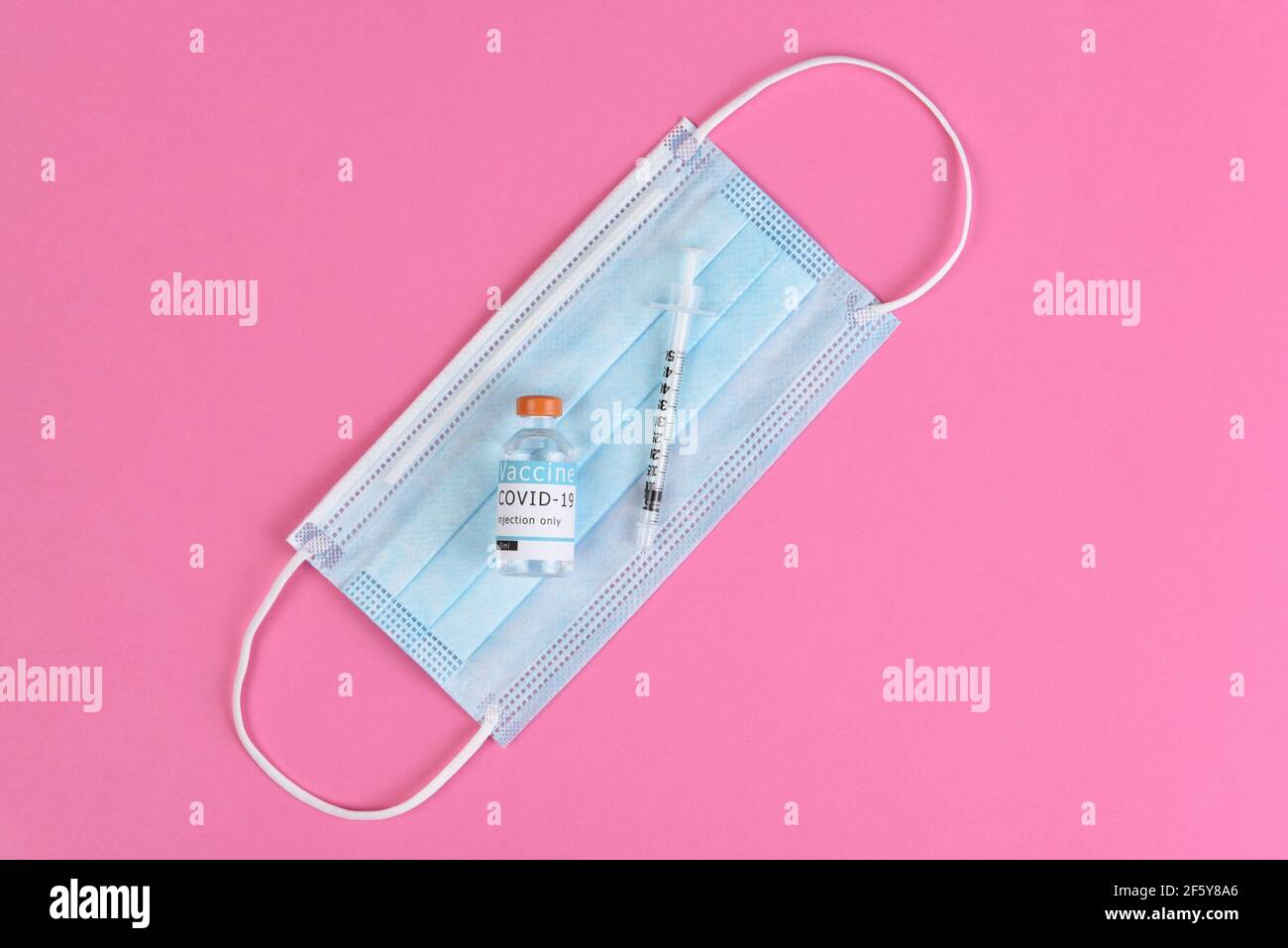 Equipment to administer a Covid19 Vaccination. Flat lay with surgical mask, syringe and vaccine vial, on pink background. Stock Photo