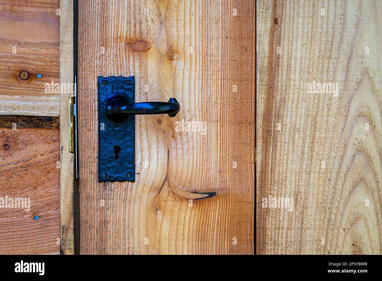 Closeup of black wrought iron door handle on waney edge wooden shed door. Stock Photo