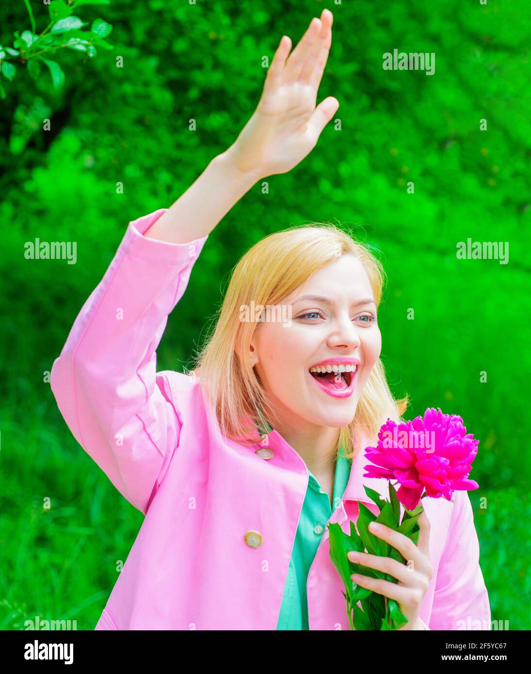 Springtime. Happy woman with peony flower waving hand. Smiling girl welcoming to friends. Stock Photo