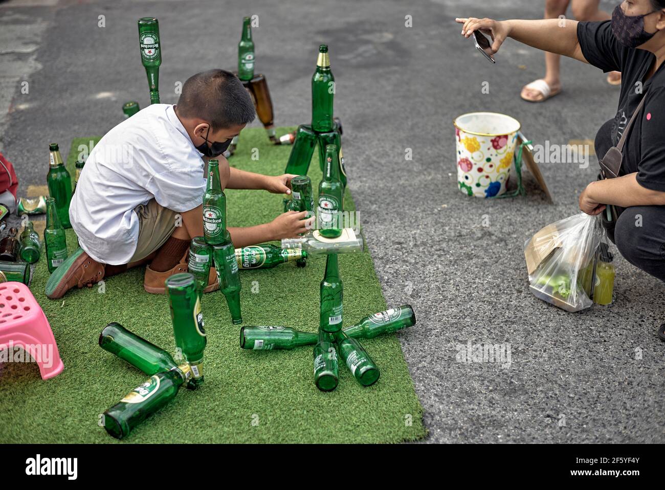 Imaginative child. Young boy arranging and balancing beer bottles trick to earn money on the street. Thailand, Southeast Asia Stock Photo