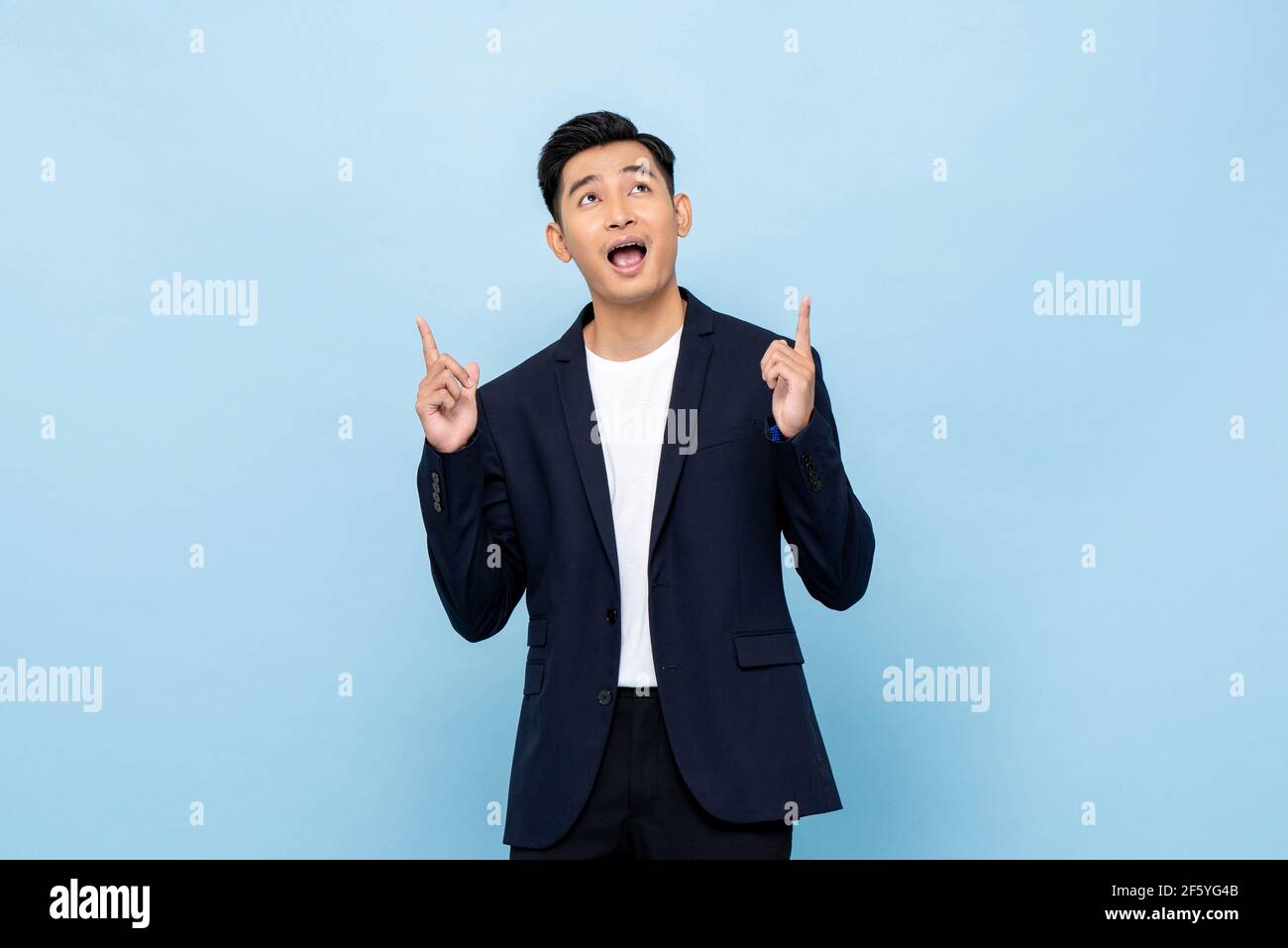 Young handsome southeast Asian businessman pointing hands and looking upward on light blue studio background Stock Photo