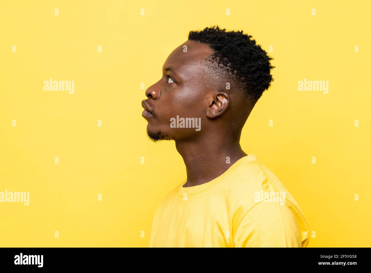 Side view shot of young African man face on isolated yellow studio background Stock Photo