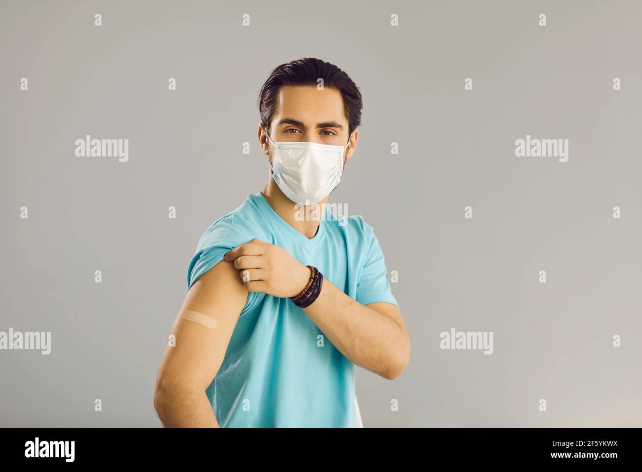 Close up on gray background man in medical mask shows hand with patch at vaccine injection site. Stock Photo