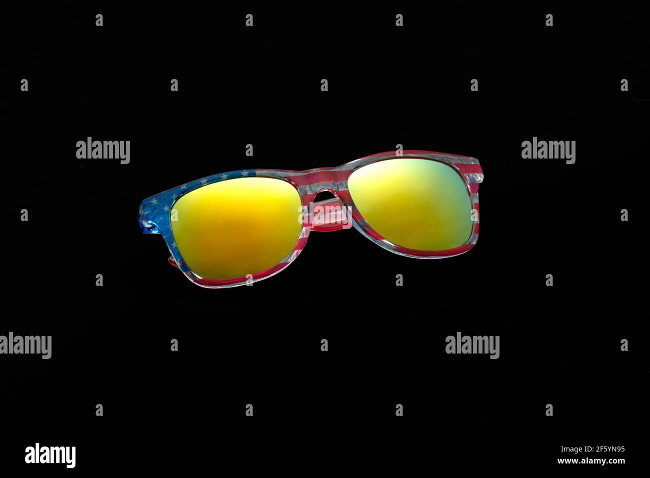 Sunglasses with chameleon mirror glasses in frame with print of flag of America isolated on black background. Travel to United States. Stock Photo