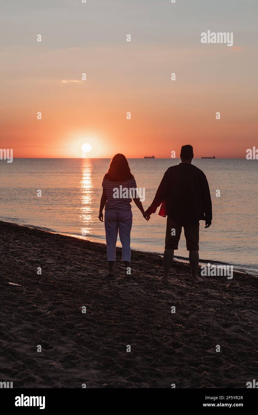 couple holding hands looking at sunset above sandy sea Stock Photo - Alamy