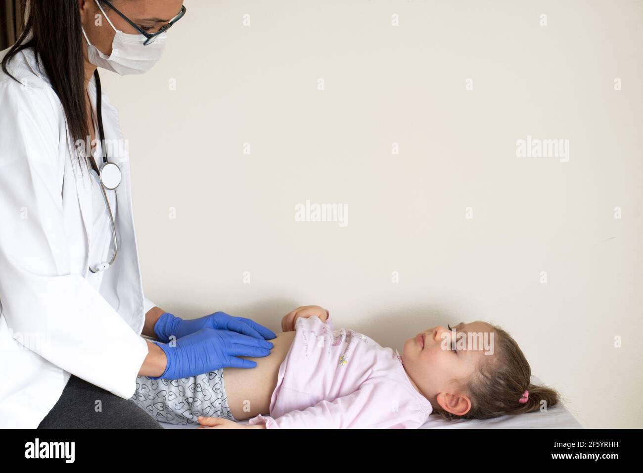 chubby little girl in pediatric examination by her doctor. Doctor examining the abdominal internal organs. Space for text, copy space, empty space bac Stock Photo