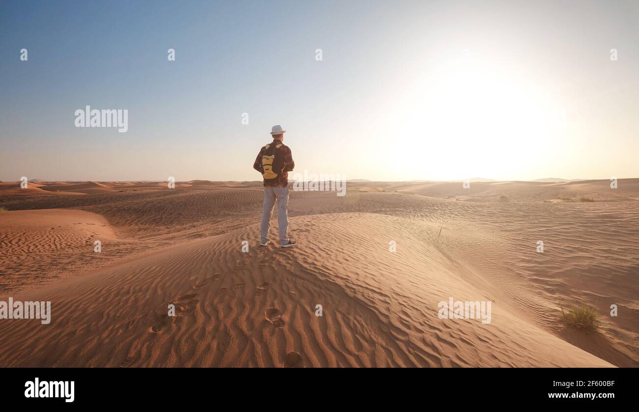 Desert adventure. Young man with backpack walking on sand dune. The ghost town of Al-Madam near Dubai, United Arab Emirates. idea and concept of succe Stock Photo