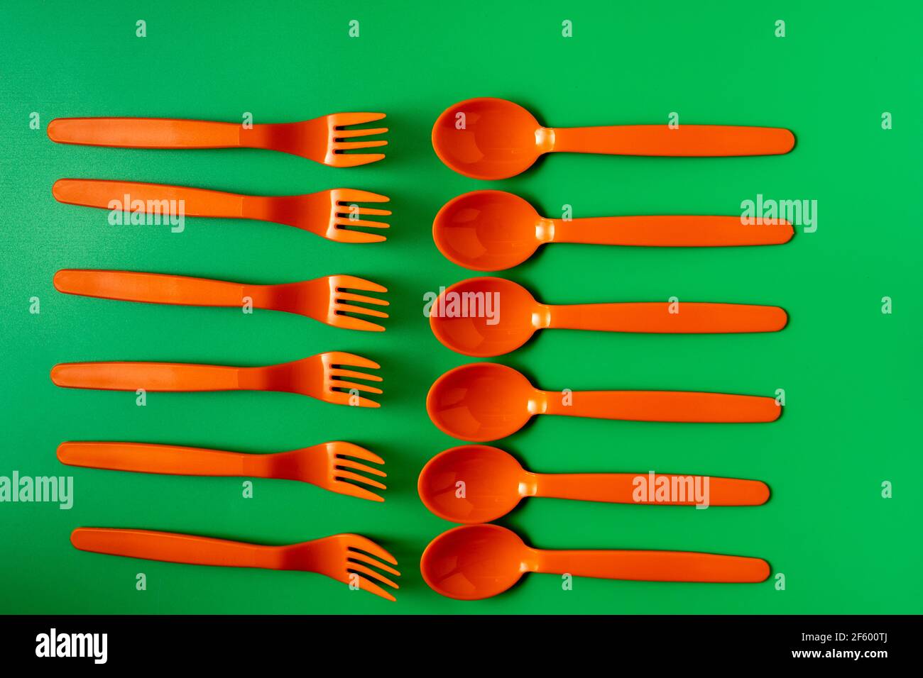 Plastic orange spoons and forks on green background. Eco friendly and