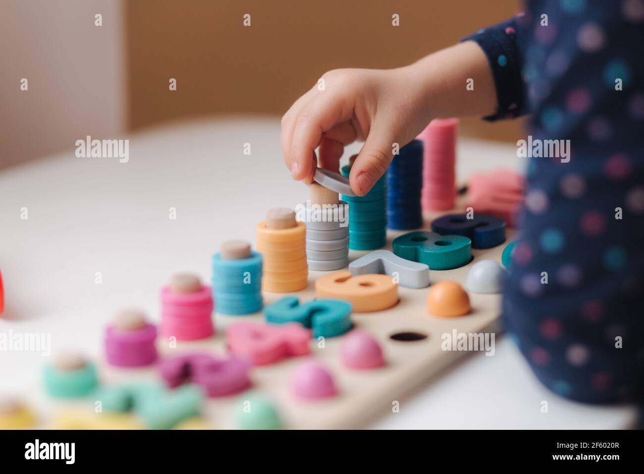 Closeup of kid's hand putting color rings on wooden column. Little girl ...