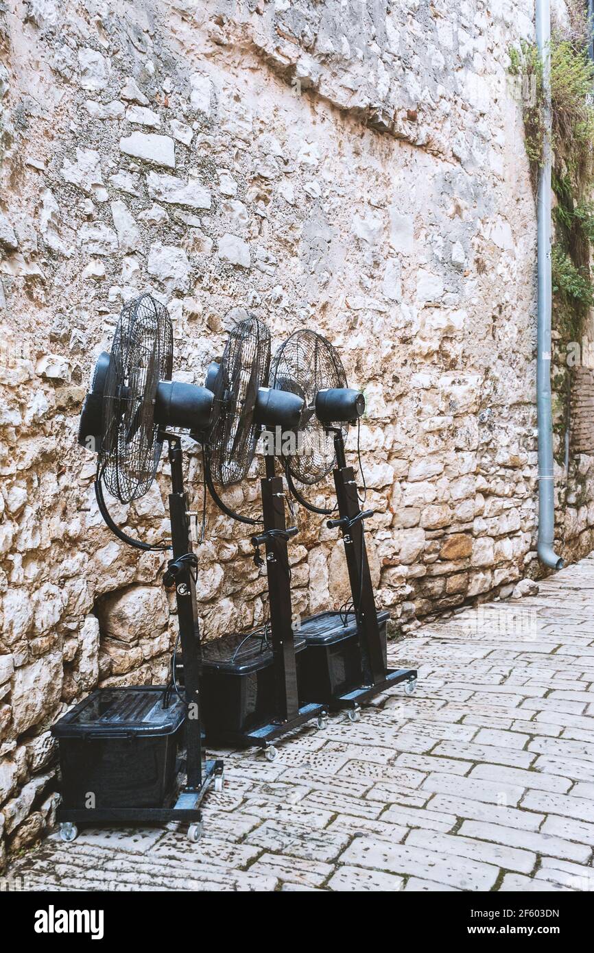 Electric black fans stand against a stone wall in a European city. Cooling devices on the street of the city. Stock Photo