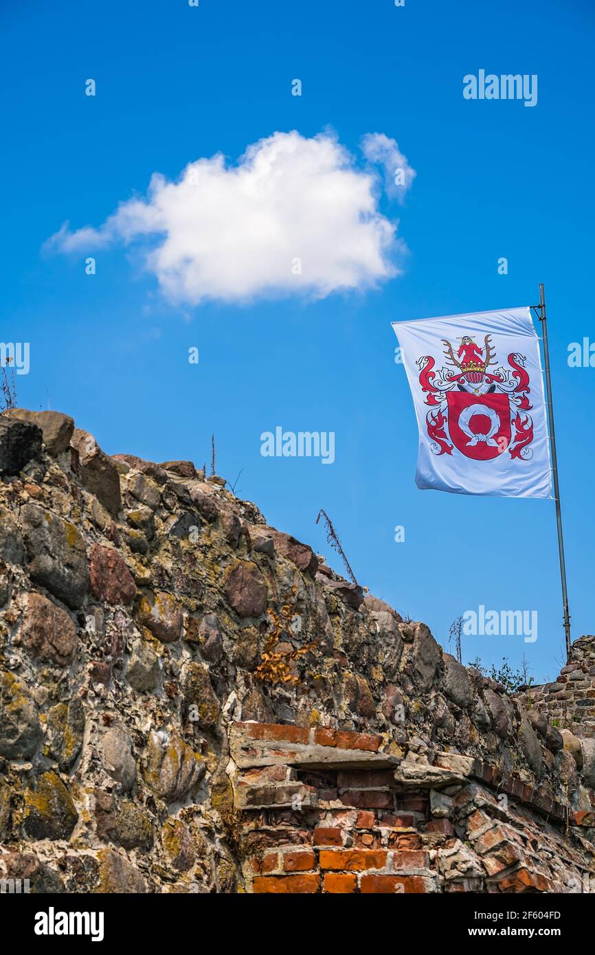 Wenecja, Poland - July 2020 : Flag fluttering on a mast above the ruins of Wenecja castle in a field under the sunlight and a blue sky Stock Photo