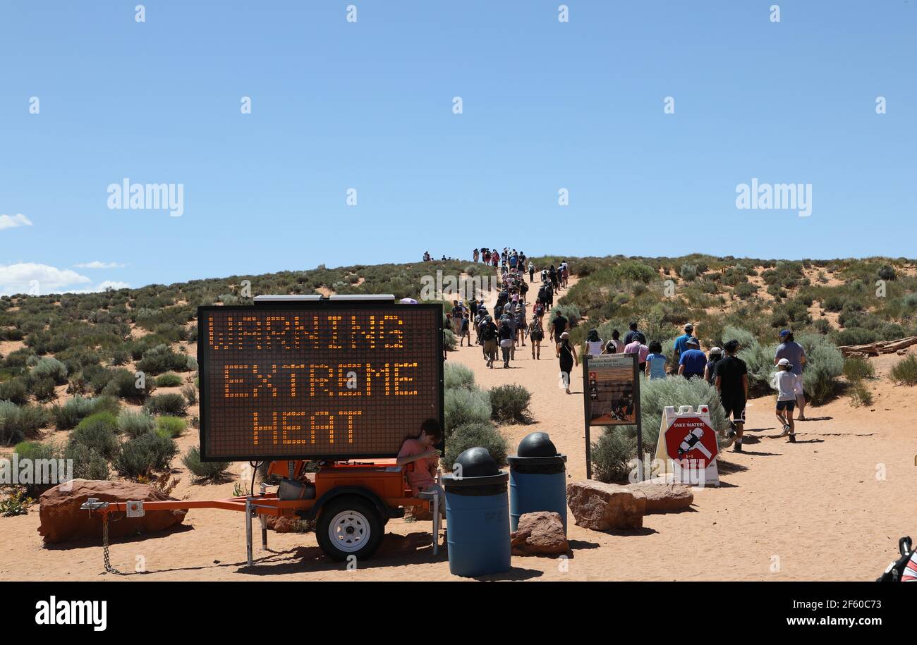 Procession of people passing a sign that warns for extreme heat;they are nevertheless following each other towards the horizon; global warming concept Stock Photo
