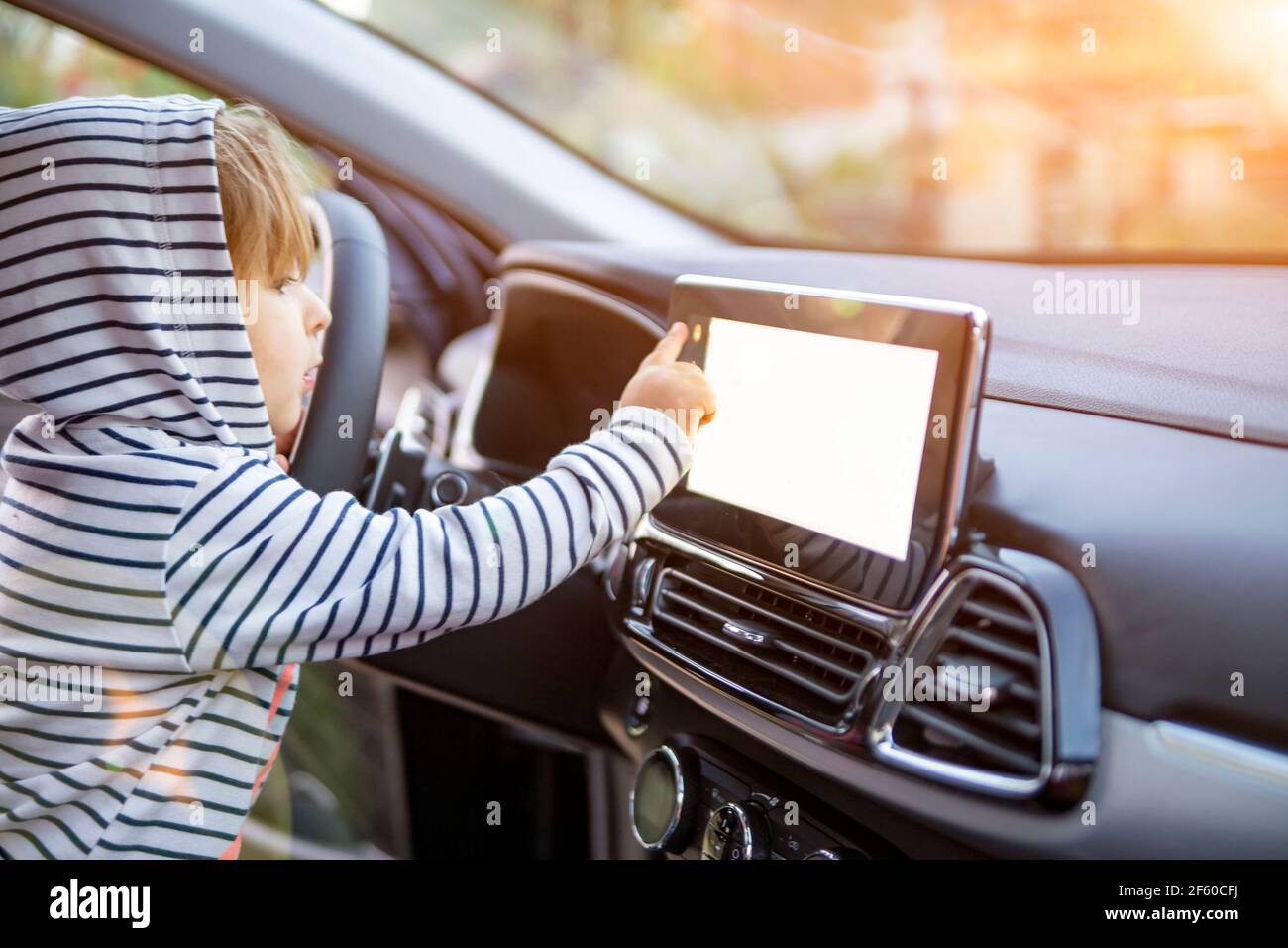 curious toddler girl holding, touching, and turning a car mnultiedia touch screen player button. empty white screen Stock Photo