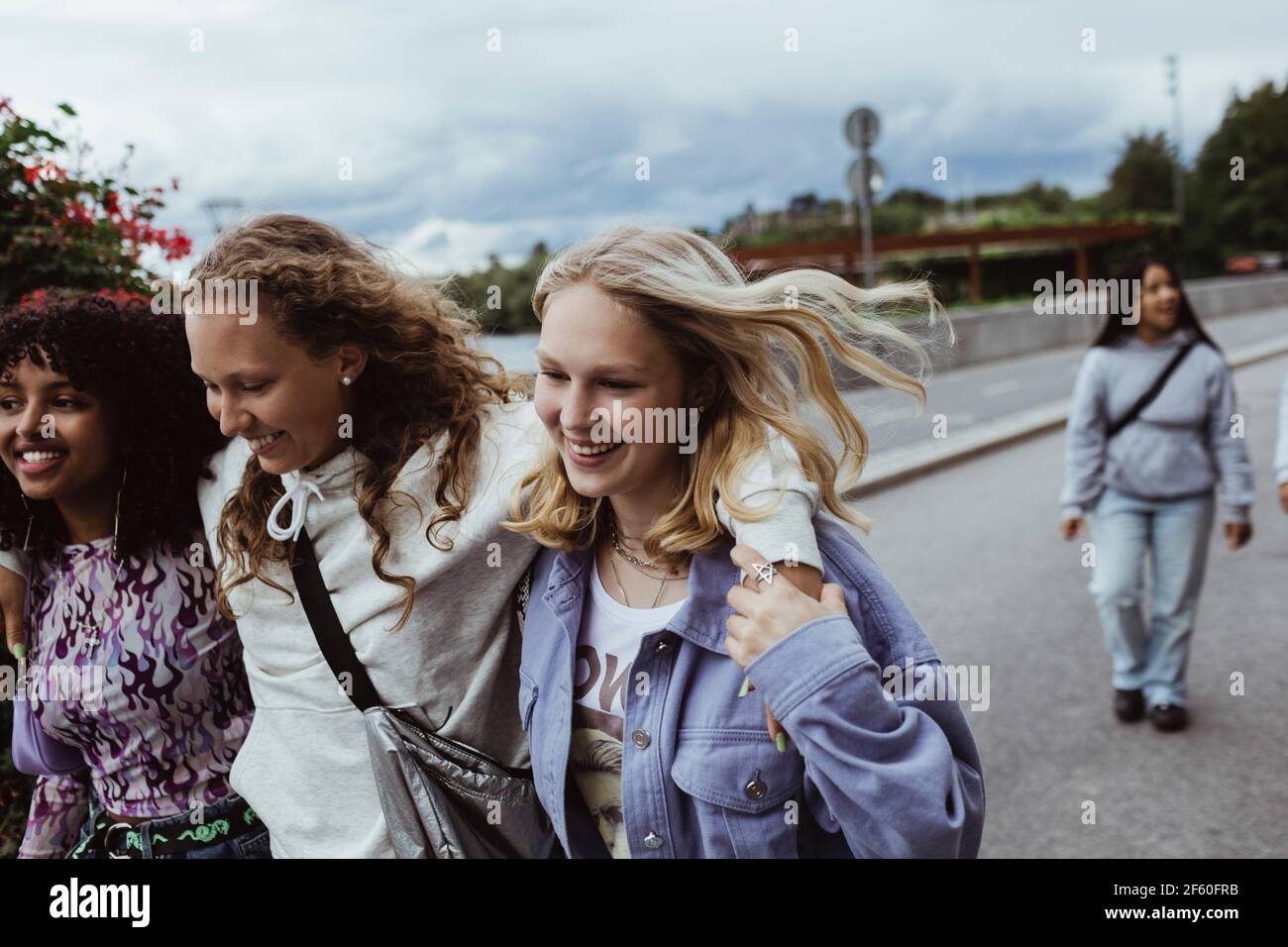 Smiling friends with arms around walking on footpath against sky Stock Photo