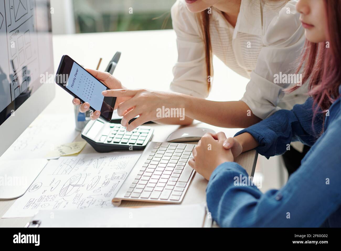 Entrepreneur showing calendar on smartphone screen to young UI designer