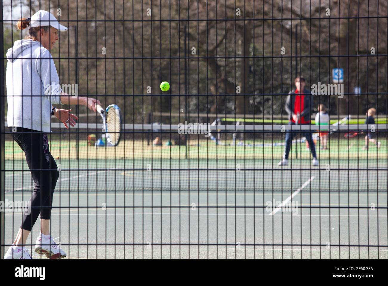 London, UK, 29 March 2021: On Tooting Commons a woman plays tennis, which from today is permitted under the gradual easing of lockdown rules in England. Anna Watson/Alamy Live News Stock Photo