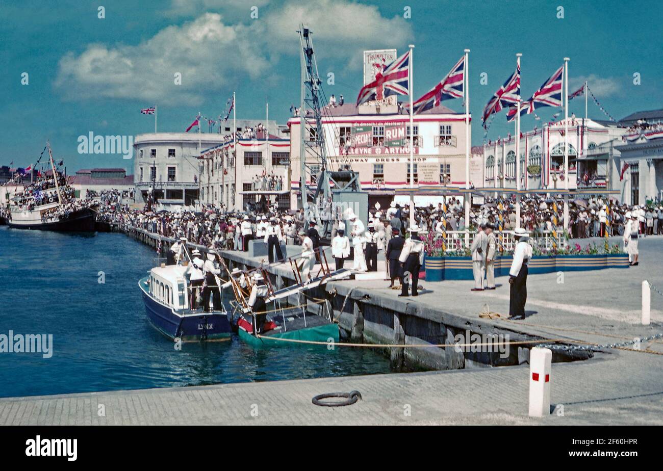 Crowd scenes in Bridgetown, Barbados, 1955, during Princess Margaret’s Caribbean tour. Here crowds line the harbour at Trafalgar Square (now called National Heroes Square). Dignitaries are boarding the tender, ‘Lynx’, to be ferried out to the moored Royal Yacht ‘Britannia’. In January 1955, the Princess made the first of many trips to the Caribbean, her tour aboard Britannia to the British colonies was popular throughout the West Indies. Princess Margaret, (1930 – 2002) was the sister of Queen Elizabeth II. This image is from an old amateur 35mm colour transparency – a vintage 1950s photograph Stock Photo