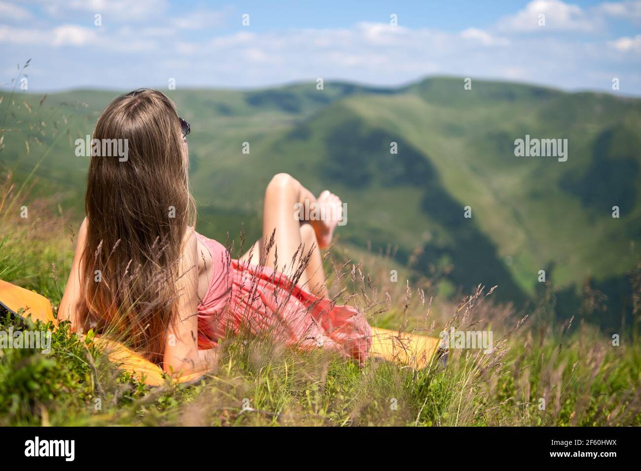 Young woman in red dress lying down on green grassy meadow on a warm