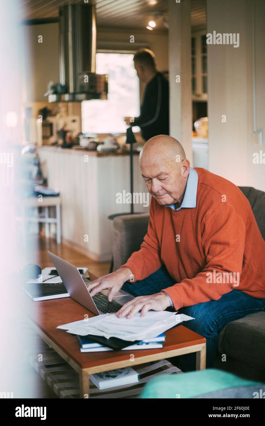 Elderly gay man using laptop while calculating financial bill at home Stock Photo