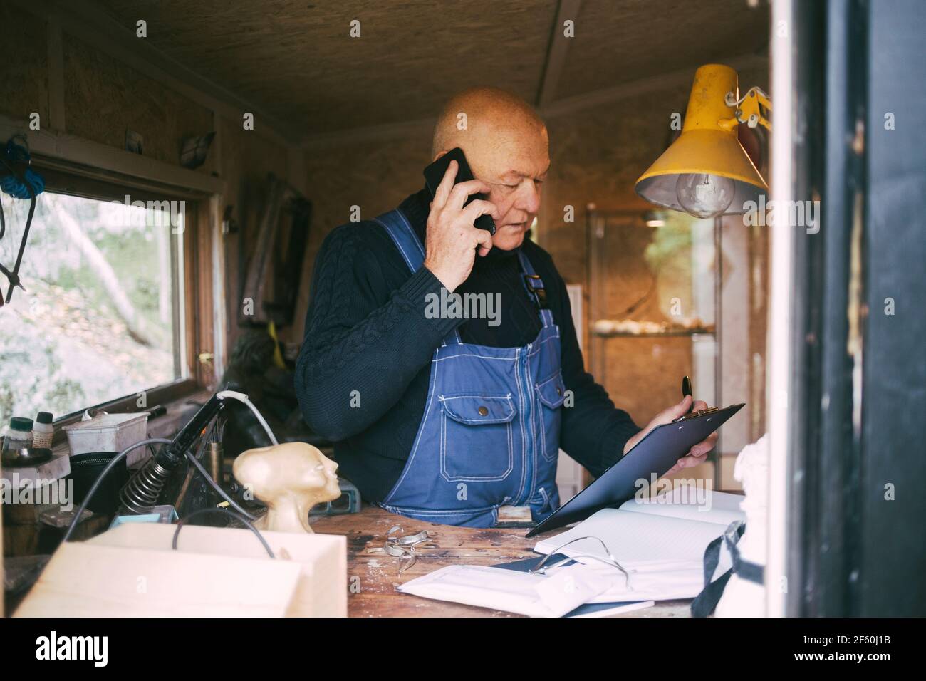 Senior businessman talking on mobile phone while looking at clipboard at garage Stock Photo