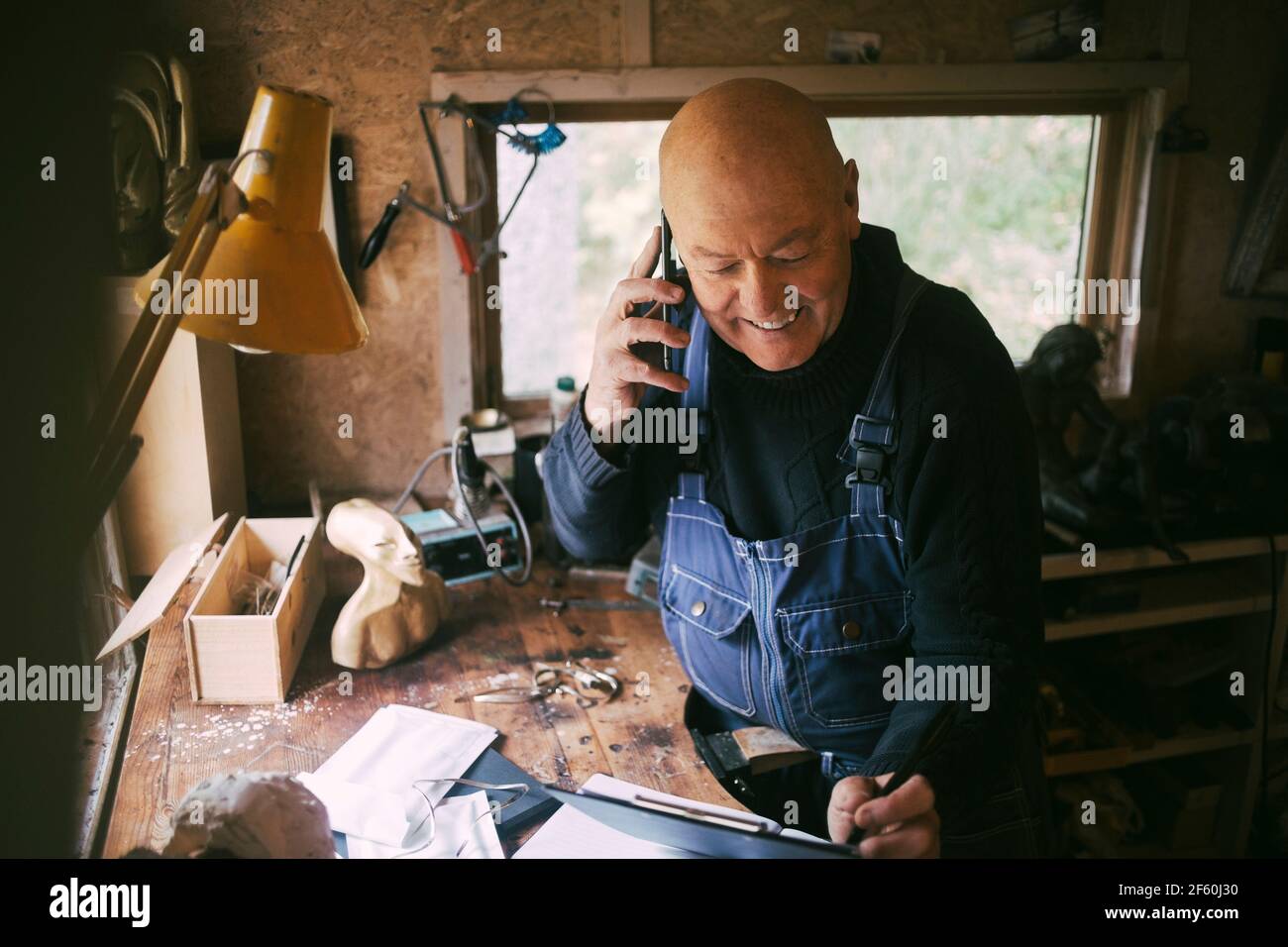 Smiling businessman talking on smart phone in workshop Stock Photo