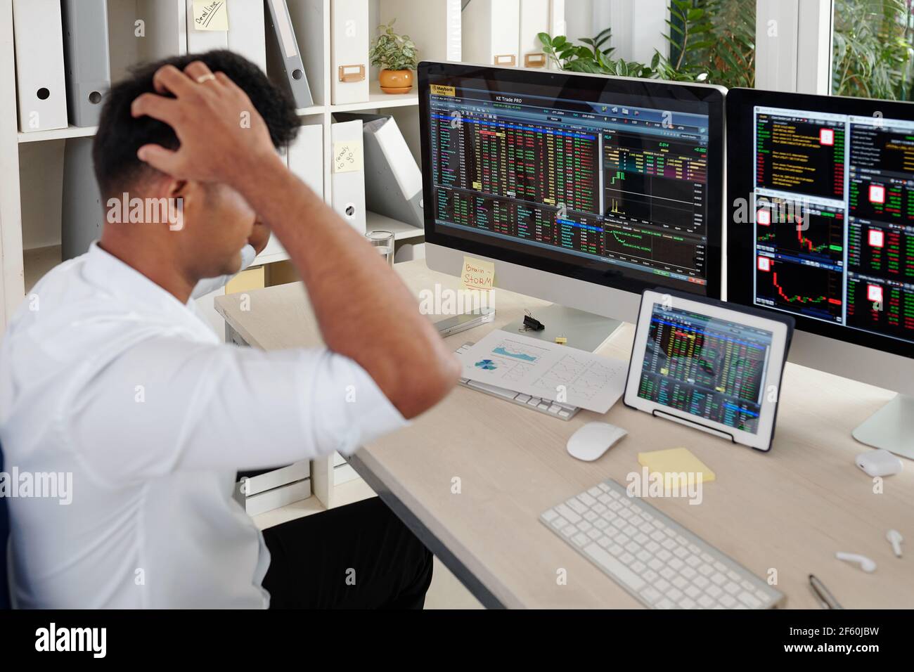 Stressed trader touching head when looking at computer screens with stock market data Stock Photo