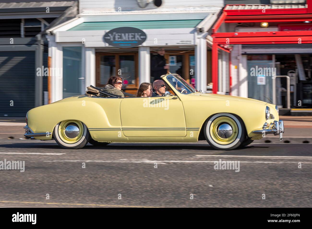 Southend on Sea, Essex, UK. 29th Mar, 2021. The first day of the UK’s easing of lockdown has cleared into a bright and sunny day, though remaining cool. 1962 Volkswagen Karmann Ghia classic car driving past arches restaurants Stock Photo