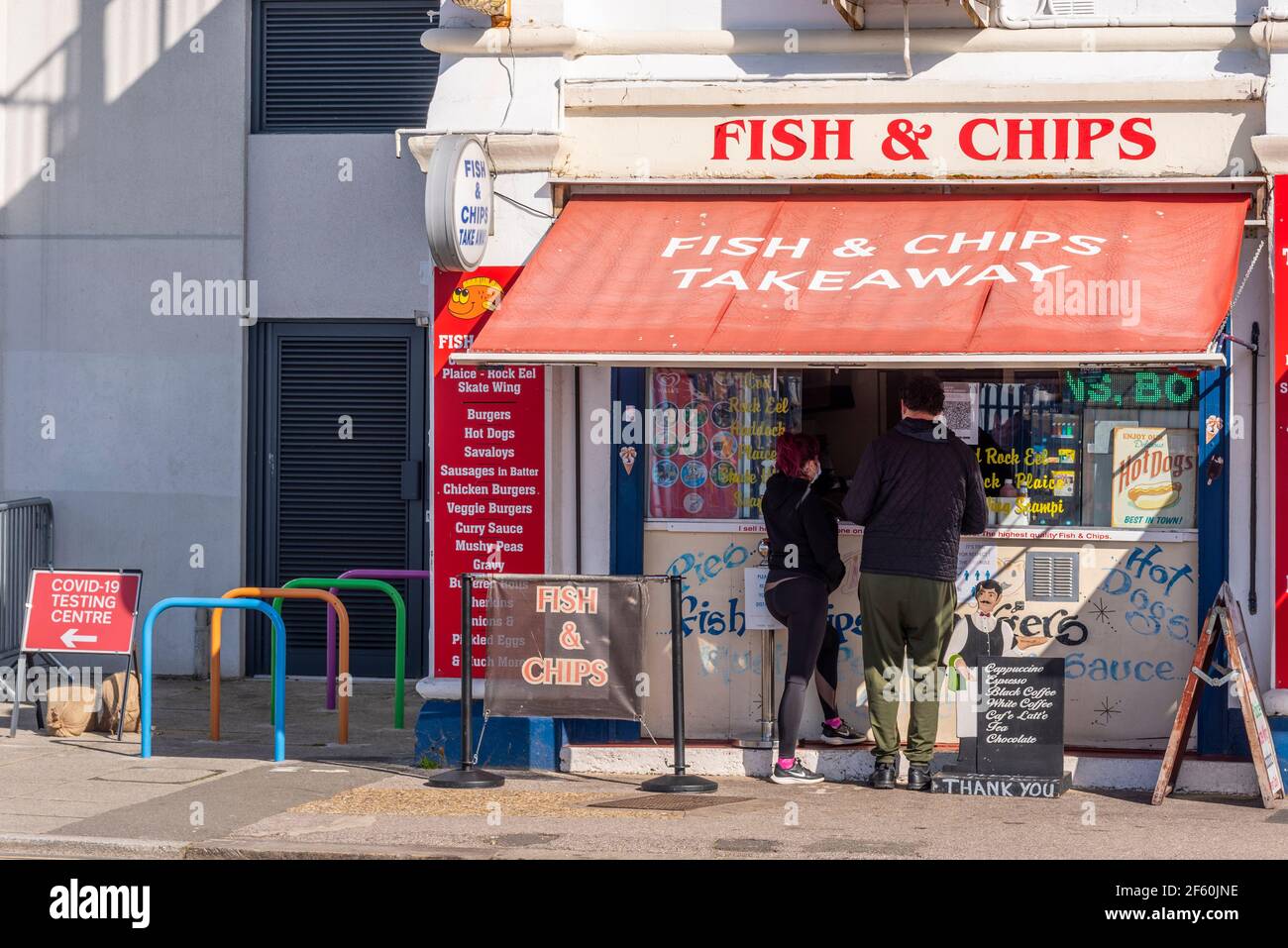 Southend on Sea, Essex, UK. 29th Mar, 2021. The first day of the UK’s easing of lockdown has cleared into a bright and sunny day, though remaining cool. Seafront cafes are open for take-away business. Fish & Chips takeaway shop with customers. Sign for COVID 19 testing centre next door Stock Photo