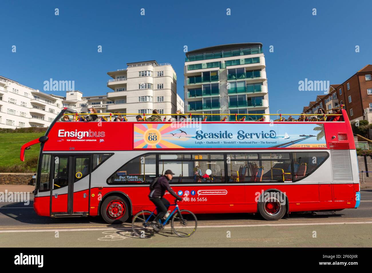 Southend on Sea, Essex, UK. 29th Mar, 2021. The first day of the UK’s easing of lockdown has cleared into a bright and sunny day, though remaining cool. Ensignbus have commenced their seafront 'Seaside Service' open top bus service. Passengers on top deck passing seafront properties. Cyclist in cycle lane Stock Photo