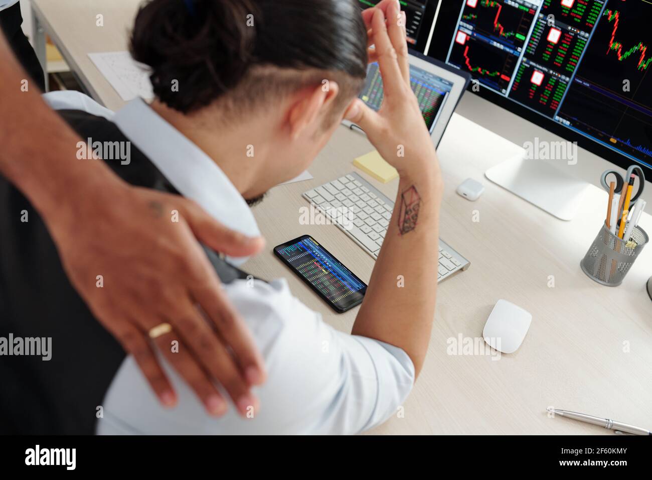 Trader supporting colleague monitoring stock market via application on smartphone Stock Photo