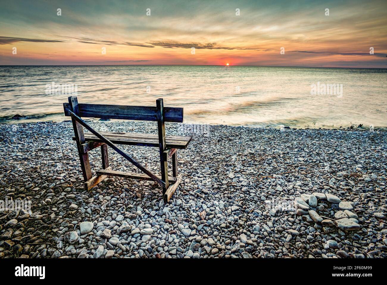 An empty bench watch's a warm spring sunset on the bay of Green Bay located on the door country peninsula in Wisconsin. A popular tourist destination Stock Photo