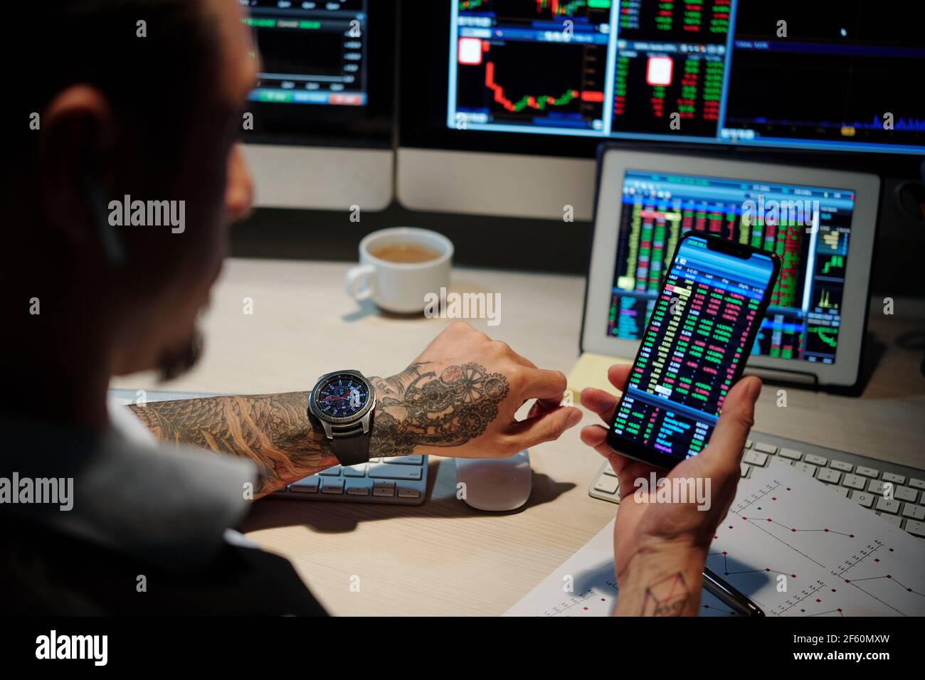Trader working late at night and checking stock markets data via application on smartphone Stock Photo