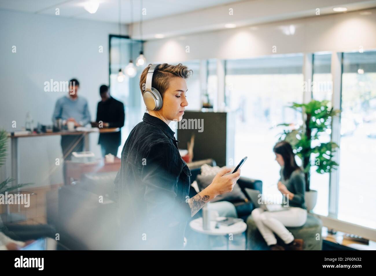 Female entrepreneur using smart phone while colleagues working in background Stock Photo