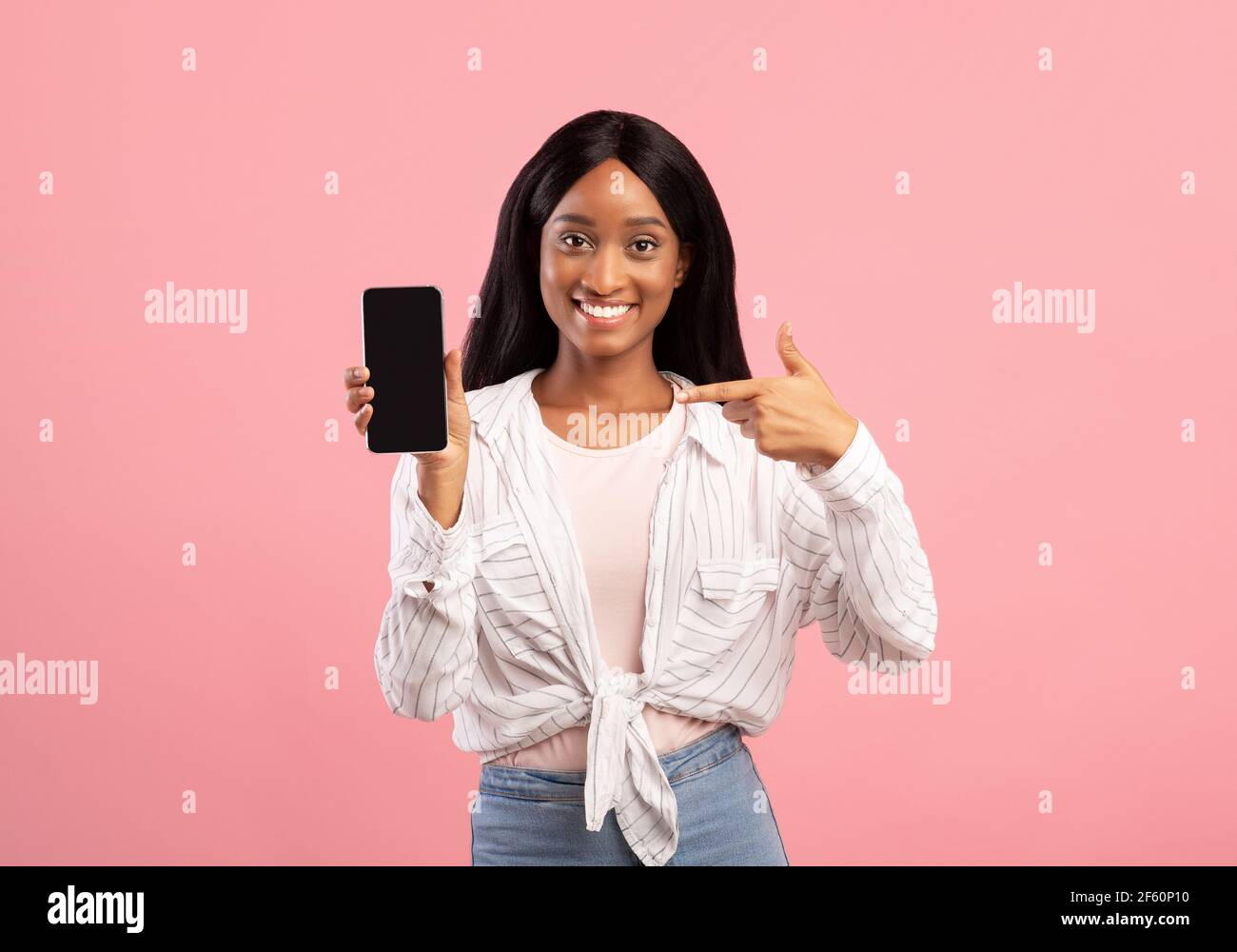 Black woman pointing at cellphone with blank screen on pink background ...