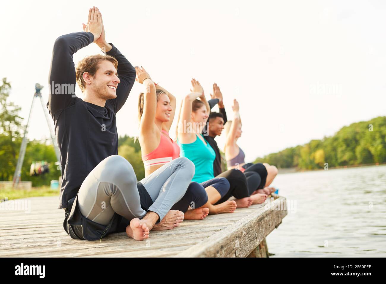 Friends doing yoga exercise together on the lakeside for relaxation and health Stock Photo