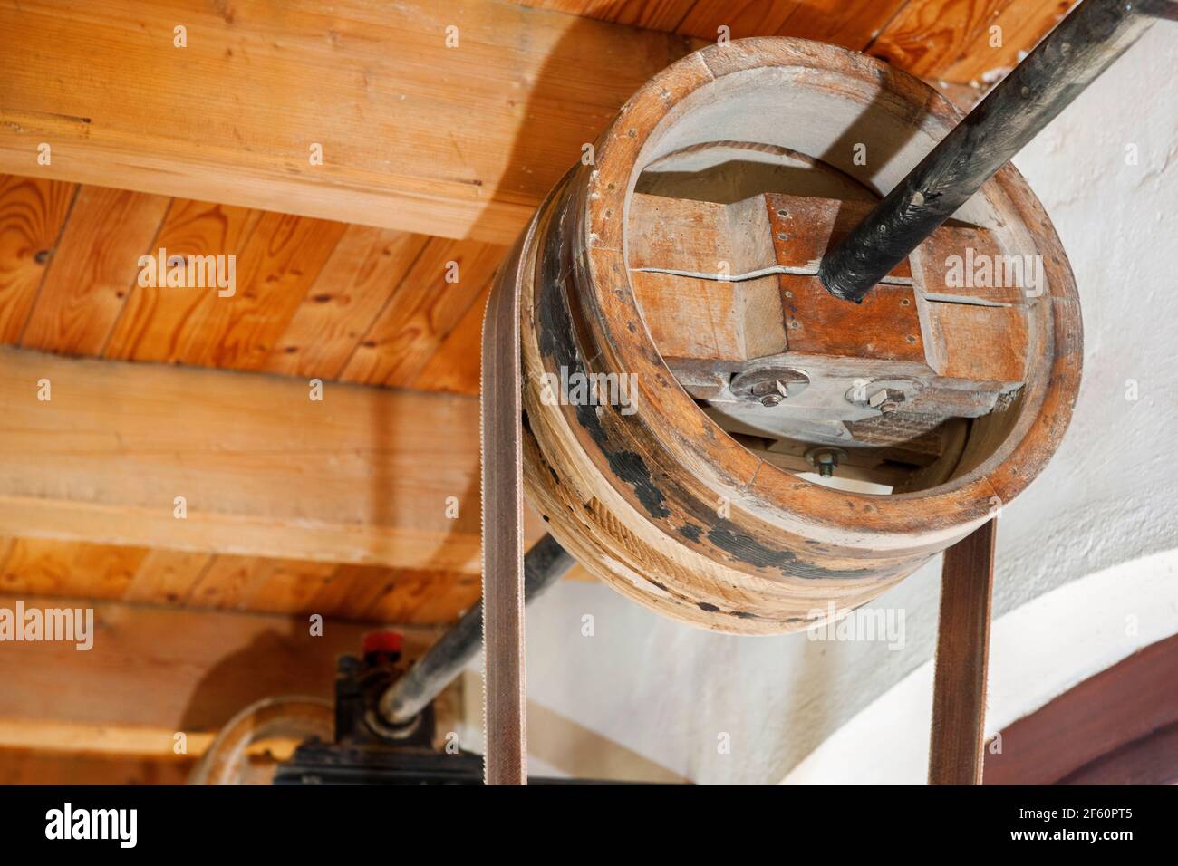 Old wooden wheel on a shaft as part of a transmission drive under the ceiling beams of an old carpenter's factory. Stock Photo