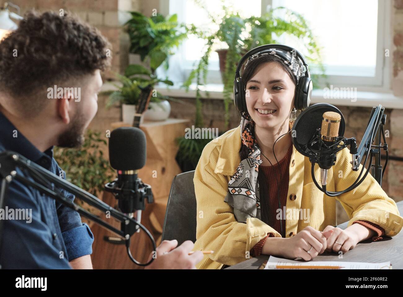 Young woman in headphones giving an interview to young man during broadcasting at radio studio Stock Photo