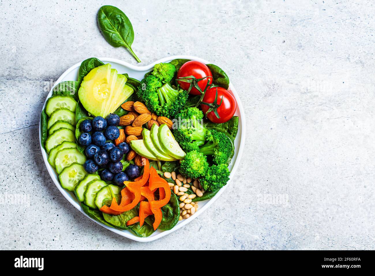 Healthy heart diet concept. Salad with vegetables, olive oil, berries and nuts in a heart plate
