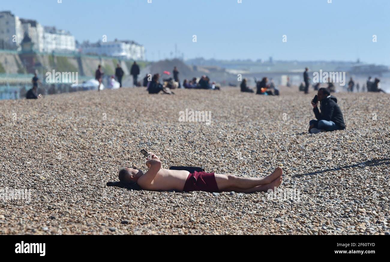 Brighton UK 29th March 2021 - A sunbather enjoys a lovely sunny day on Brighton beach as lockdown restrictions have started to ease in England  Temperatures are expected to reach the mid 20s in some parts of the South East over next few days. : Credit Simon Dack / Alamy Live News Stock Photo
